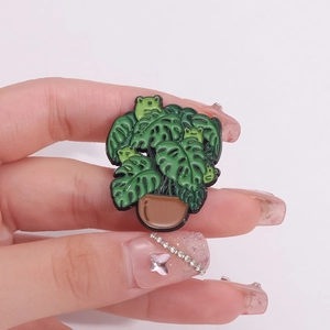 Creative enamel monstera plant brooch featuring small cartoon frogs on green leaves