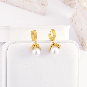 Detail of elegant gold drop earrings featuring white teardrop pearls on a stone background