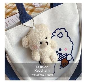 Close-up of white plush bear pendant with silver chain on a cloud print canvas bag