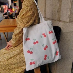 Close-up of white canvas tote bag with red cherry print worn on a female shoulder