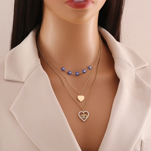 Close-up of golden triple-layer necklace with blue evil eye and heart charms on model
