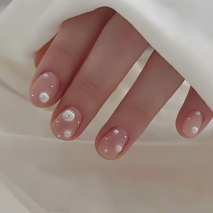Faux ongles courts avec perles et strass sur base rose doux portés sur la main