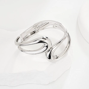 Close-up of a silver open cuff bracelet with cross lines and spring hinge on a stone surface