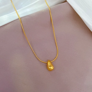 Detail of a gold waterdrop pendant on a sleek snake chain over soft silk fabric
