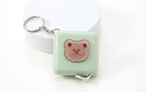Detail of green square retractable tape measure with brown bear icon and metal keychain