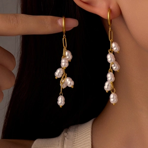 Elegant gold-tone baroque pearl cluster tassel earrings on model with black background
