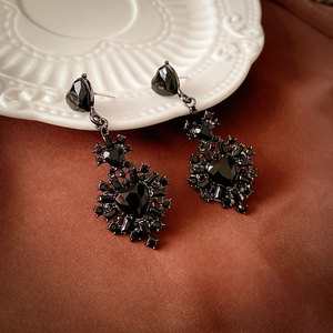Detailed view of gothic heart earrings with black stones hanging on a relief plate