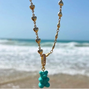 Macro shot of a golden heart chain necklace with a blue gummy bear resin pendant at the beach