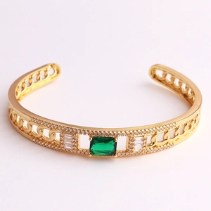 Detail view of gold geometric bracelet with green rectangular zircon and crystal accents