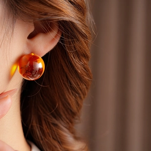 Detailed close-up of amber resin round earrings worn by model for retro autumn fashion