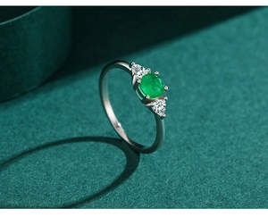 Macro view of three-stone silver ring with round green emerald and pear-cut side diamonds