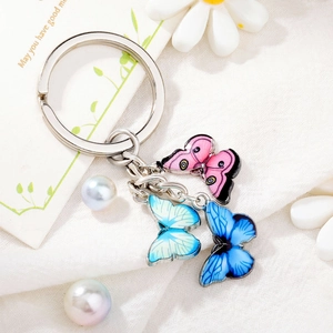 Detailed view of silver metal keychain with pink and blue enamel butterfly charms on fabric