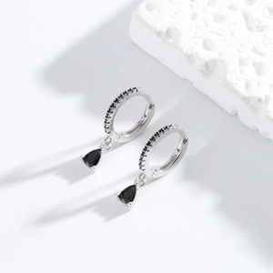 Detail of silver hoop earrings with black micro-diamonds and pear-shaped drop charms