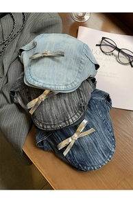 Three colors of denim beret hats with silver bows and pink gems on a wooden desk