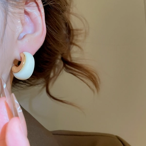 Close-up of 18k gold-plated C-shaped resin earring worn on a model ear in warm light