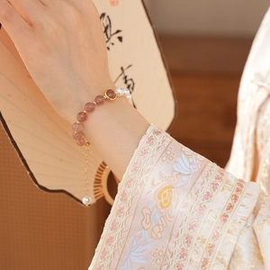 Detail of strawberry quartz and pearl bracelet worn with traditional Chinese embroidery