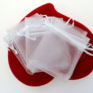 Close-up of white organza drawstring bags stacked on a red heart velvet base for gifts