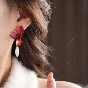 Close-up of red metal flower earrings with white water-drop pearls on a model