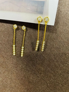 Détail de boucles d'oreilles pendantes dorées avec pierres rondes sur fond en feutre brun