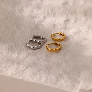 Detail of flower-shaped wave gold and silver hoop earrings on textured background