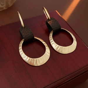 Detail of gold hammer-textured metal rings and dark brown leather hoop earrings