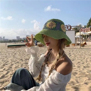 Close-up of hand-crocheted green straw bucket hat with yellow sunflower detail in beach setting