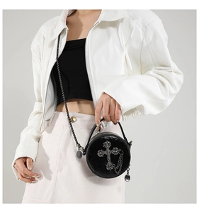 Close-up of gothic silver cross and metal chain detail on round black leather bag