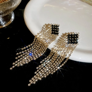 Macro shot of gold tassel earrings with black and white rhinestones on white ceramic