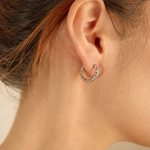 Close-up of textured silver hoop earrings with a sophisticated braided finish on ear