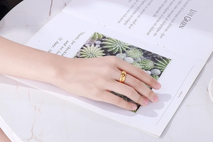 Primo piano di un anello dorato con trama a foglia indossato sul dito indice