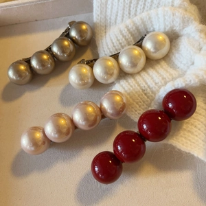 Close-up of four minimalist pearl hair clips in champagne, cream, pink, and deep red colors