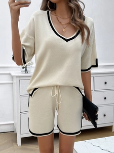 Close-up of beige V-neck knitted set with black contrast trim and elegant gold jewelry