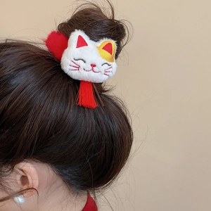Detail view of plush Maneki Neko hair tie with red tassels on a model's ponytail