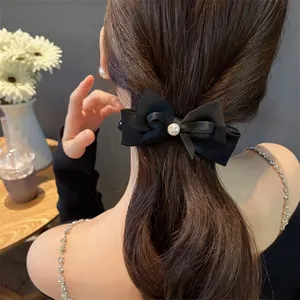 Elegant black velvet bow hair clip with pearl detail shown on a ponytail hairstyle