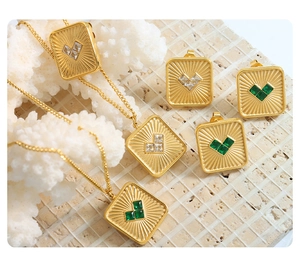 Close-up of gold square pendants with heart zirconia inlays on textured stone surface