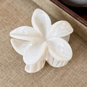 Macro shot of a pearlescent white plumeria flower hair claw clip on woven fabric