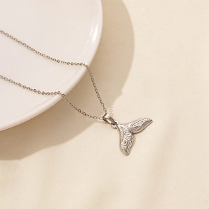 Detail of silver whale tail pendant with sea textures on a minimalist fabric background
