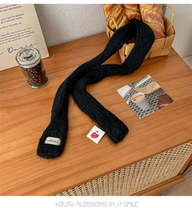 Close-up of black knitted skinny scarf with white brand label on wooden tabletop