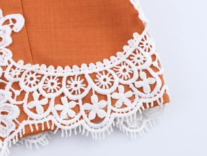 Macro detail of elegant orange fabric with intricate white lace embroidery and fringe trim