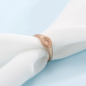 Detailed close-up of rose gold signet ring with engraved star on white fabric texture