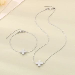 Silver stainless steel cross pendant necklace and bracelet jewelry set on beige fabric
