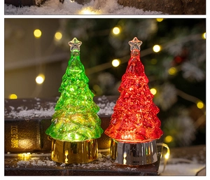 Close-up of green and red LED crystal Christmas trees on snow-covered books with warm lights