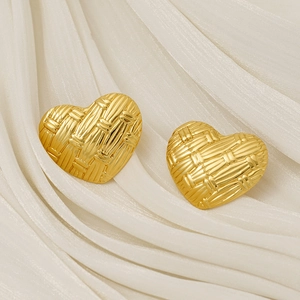 Textured golden heart-shaped stud earrings on soft beige pleated fabric backdrop
