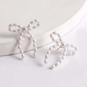 Close-up of handmade pearl bow earrings with golden wire and white oval pearls