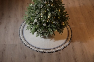 Close-up of beige knitted Christmas tree skirt with grey patterns and tassel fringe edge