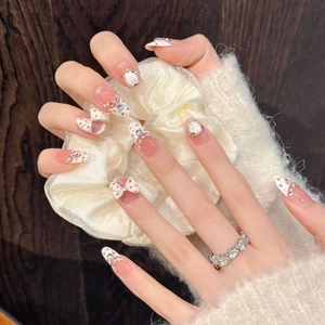 Detail of luxury press-on nails with 3D bows, pearls, and crystals on almond-shaped tips
