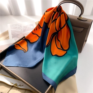 Elegant floral silk square scarf in orange and navy blue draped on a leather handbag