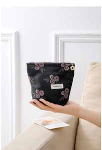 Close-up of black jacquard makeup bag with red rose embroidery and gold flower zipper pull