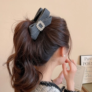 Detail of dark grey fabric bow hair clip with rhinestone buckle on model hairstyle