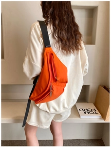 Detail of bright orange crossbody bag with multi-layer zippers and wide black strap